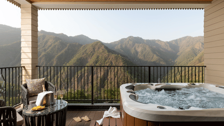 A private balcony featuring a bubbling outdoor hot tub and a seating area overlooking spectacular mountain ridges.