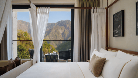 Four-poster bed with white linens and drapes facing glass doors that open to mountain views.