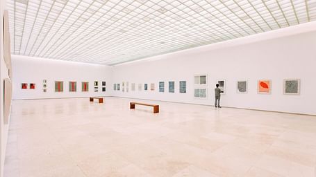A solitary person looking at a painting in a museum that has painting across the wall.