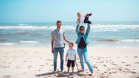 A family of four posing on the beach with white sands and blue sky in the background