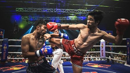 two muay thai fighters fighting inside a ring with a referee behind them officiating