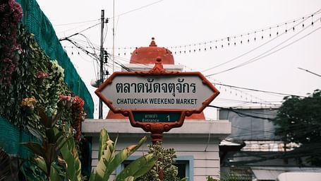 a signage of Chatuchak Weekend Market at the entrance of the event space with white clouds in the background