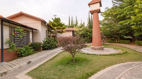 Lush garden with pathway and central pillar near cottages at Nirantara Resort & Spa