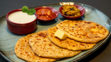 Stuffed Punjabi parathas served with curd, pickle, and chutney on a platter.