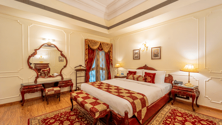 The luxurious bedroom area of the Presidential Suite at Noor-Us-Sabah Palace, featuring a king-sized bed with red and gold checkered linens, a classic vanity with a large ornate mirror, and warm ambient lighting.