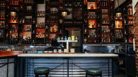 A bar with chairs, glasses, and bottles arranged in shelves.