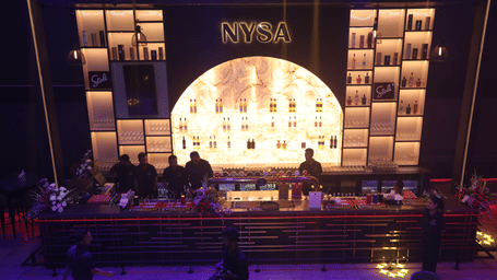 An illuminated bar with bartenders making drinks at Nysa Skybar, Bengaluru.