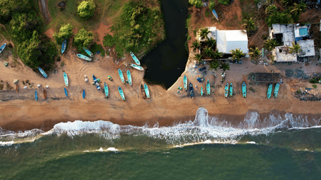 An aerial view of numerous boats parked on the shoreline of Nallavadu Beach in Pondicherry as waves gently hit the shore with a small waterbody next to the beach. A must-do on your trip is a boat ride in Pondicherry to explore the culture and nature.