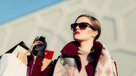 A close up shot of a woman basking in the sun holding many shopping bags.