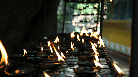 A close-up shows rows of lit oil lamps.
