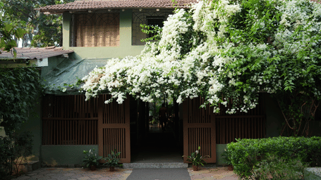 The building facade of  Oceanature Resort, Alibaug. with white flowering vines cascade over a wooden entryway