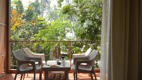 An outdoor balcony at Oceanature Resort, Alibaug featuring 4 chairs and a small table overlooking green trees.