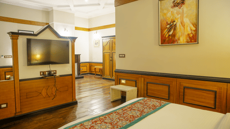 A room with a television mounted on a wall, a bed with patterned bedding, and a view into an adjacent area at Orsino Spa Resort.
