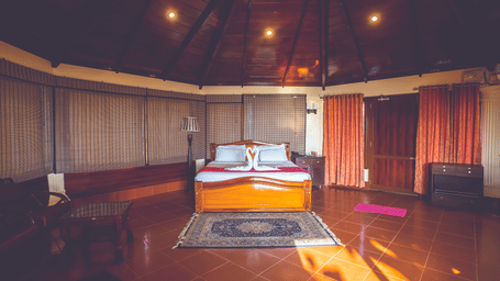 Spacious deluxe sea view cottage interior featuring a king-size bed with swan towel art, vaulted wooden ceiling, and large windows.
