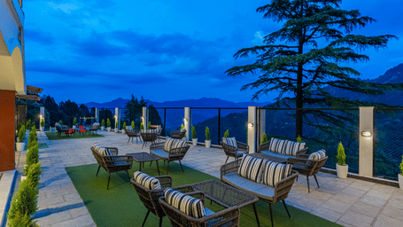 An outdoor dining area at Perfectstayz premium seven oaks, with chairs, trees, and grass mat at night.
