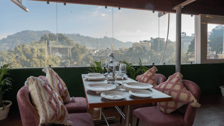 A dining area with tables and chairs overlooking mountains at Perfectstayz Premium at Mall Road Hotel Super, Mussoorie.