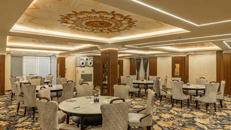 A large indoor banquet hall features round tables with grey velvet chairs on a patterned blue and gold carpet at Perfectstayz Premium Aurevva.