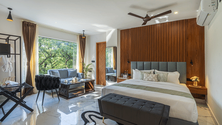 A spacious room contains a king size bed, a sofa area, and a large window showing green foliage at Perfectstayz Premium Aurevva.