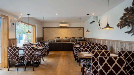 A well-lit, modern dining room featuring a patterned booth seating and wooden flooring at Perfectstayz Premium Goa Continental.
