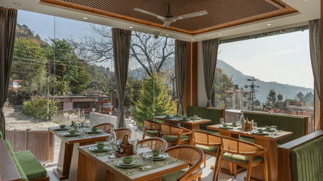 Dining room at Perfectstayz Premium Kapilaz, Bhimtal featuring wooden tables, upholstered chairs, and views of the surrounding hills.