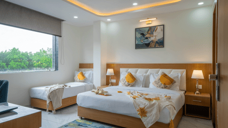 King bed with accent pillows, bedside tables, and seating area in guest room at Perfectstayz Premium Krishna Abode, Vrindavan.
