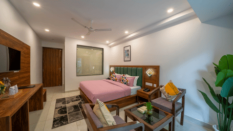 A room with a bed, a sofa with cushions, a coffee table, a wooden desk, and a wall-mounted television in Perfectstayz Premium Mystic Falls, Rishikesh.