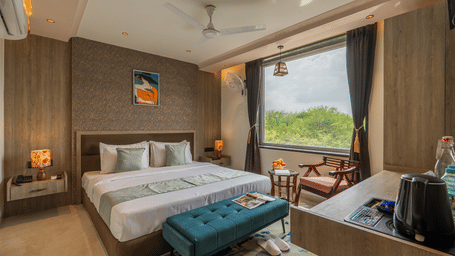 Bed with a blue ottoman at the foot and a curtained window at Perfectstayz Premium Vrindavan.