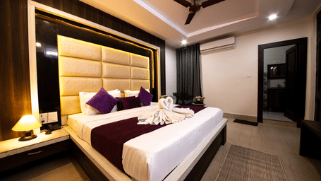 Well-lit hotel room with a large bed, dark wood panelling on the headboard wall, and modern ceiling fan - Perfectstayz Value Grey Castle, Haridwar