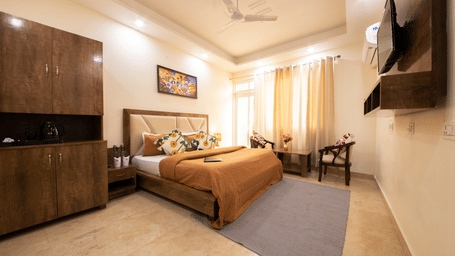 A hotel room, featuring a large bed with a brown duvet and pillows, a dark wooden headboard and nightstands, a ceiling fan, and a wall-mounted TV | Perfectstayz Value Hills, Rishikesh