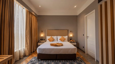 King bed with yellow cushions, marble-patterned rug and tan curtains in a guest room at Polo Hotel, Agartala.