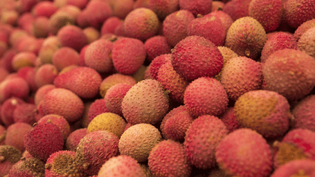 Close up of a pile of fresh pink and red lychees with textured bumpy skins stacked together at a fruit market.