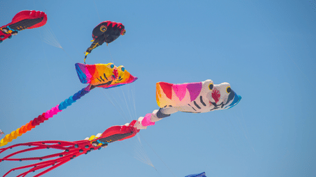 Multiples of colourful kites flying in a blue sky.