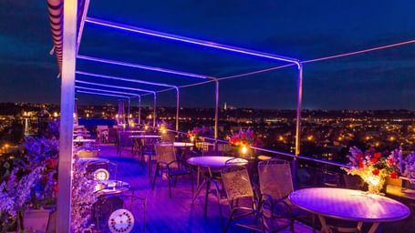 A rooftop terrace bar at night with glowing neon lights and outdoor seating.