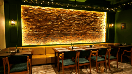  A warm dining section with a long yellow upholstered booth and a dramatic backlit stone feature wall at Pravasa Hotel, Kolhapur.