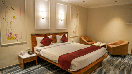 A stylish deluxe room featuring a double bed, two comfortable armchairs, and nature-inspired wall art at Pravasa Hotel, Kolhapur.
