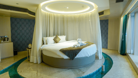 A high-end suite featuring a circular bed with a white canopy and a private surrounding water feature - Praveg's Grand Eulogia, Ahmedabad