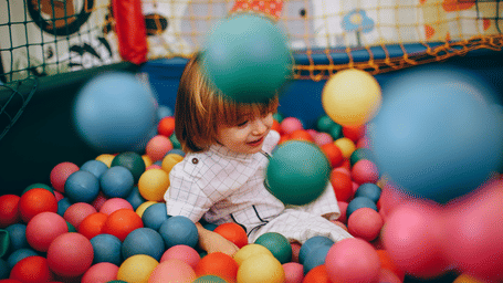 Young child sitting and playing happily in a colourful indoor ball pit.