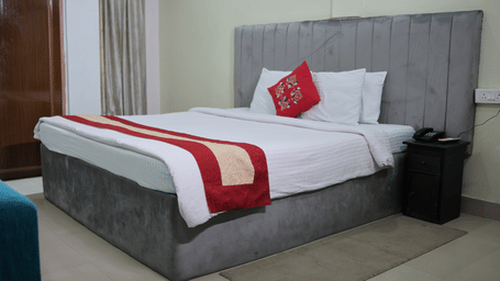 A double bed with a tall grey upholstered headboard, white bedding, and a single red accent cushion.