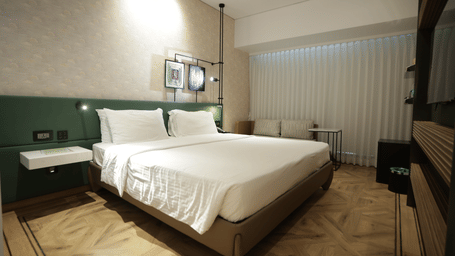 Modern guest room at Regency Hotel, Mumbai with plush bedding, contemporary furniture, large windows and elegant green accent wall for a comfortable stay.