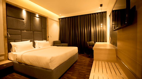 A modern hotel bedroom features a king size bed with a cushioned headboard and wooden flooring at S Hotels, Chennai.