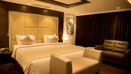 A room with a king size bed with a cushioned headboard and a small bed bench in the foreground at S Hotels, Chennai.