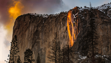 Sunlight illuminates Yosemite’s Horsetail Fall, making the water glow bright orange like lava against a dark cliff.
