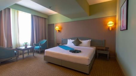  A guest room at Shilton International, Kochi, with a large bed, seating area, and a window.