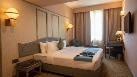 A guest room at Shilton International, Kochi, with a bed, a desk area, and a window with curtains.