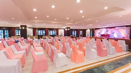 Rows of banquet chairs in white and peach covers arranged for an event in a spacious well-lit Raj Mahal at Shri Vallabh Villas Lords Plaza Nathdwara.