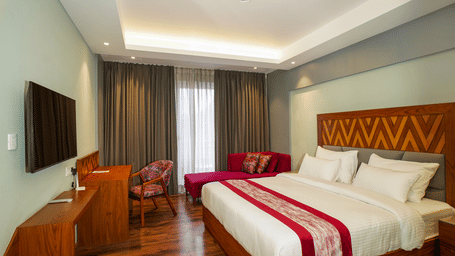 A bedroom  with a king size bed with red accents, a sofa, and a television on the opposite wall | Sukama Resort & Spa, Mukteshwar