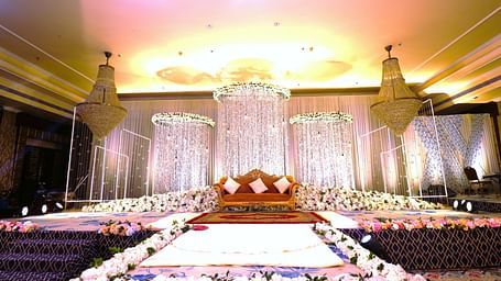 Interior view of the banquet hall stage adorned with flowers with yellow and red ambient lighting at Swosti Premium Bhubhaneswar 