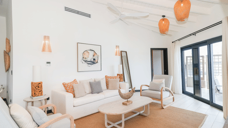 A living room at Tamarind Hills Resort and Villas - Antigua, in the Ocean 19 room, with a sofa, a sofa chair, a coffee table, entertainment center, and  pendant lighting.