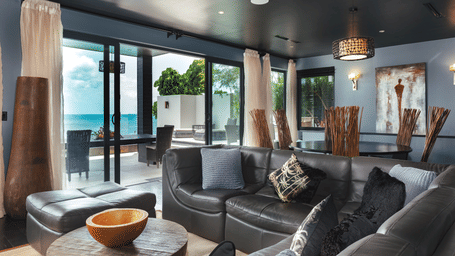 Indoor seating area with cushioned chairs and a table, overlooking the water body at Tamarind Hills Resort and Villas - Antigua.