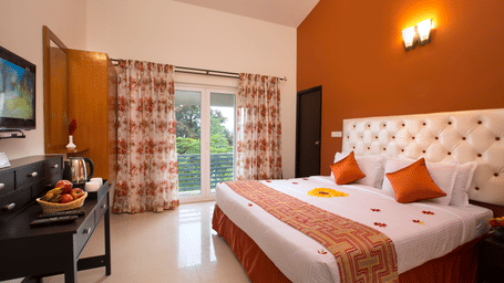 Kairos Room featuring a double bed, television, work desk with chair, window, and warm orange-themed interiors.